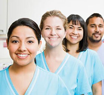 Nurses in scrubs standing in a line smiling