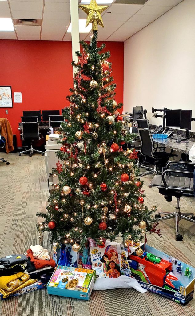 Office with presents placed underneath decorated Christmas tree.