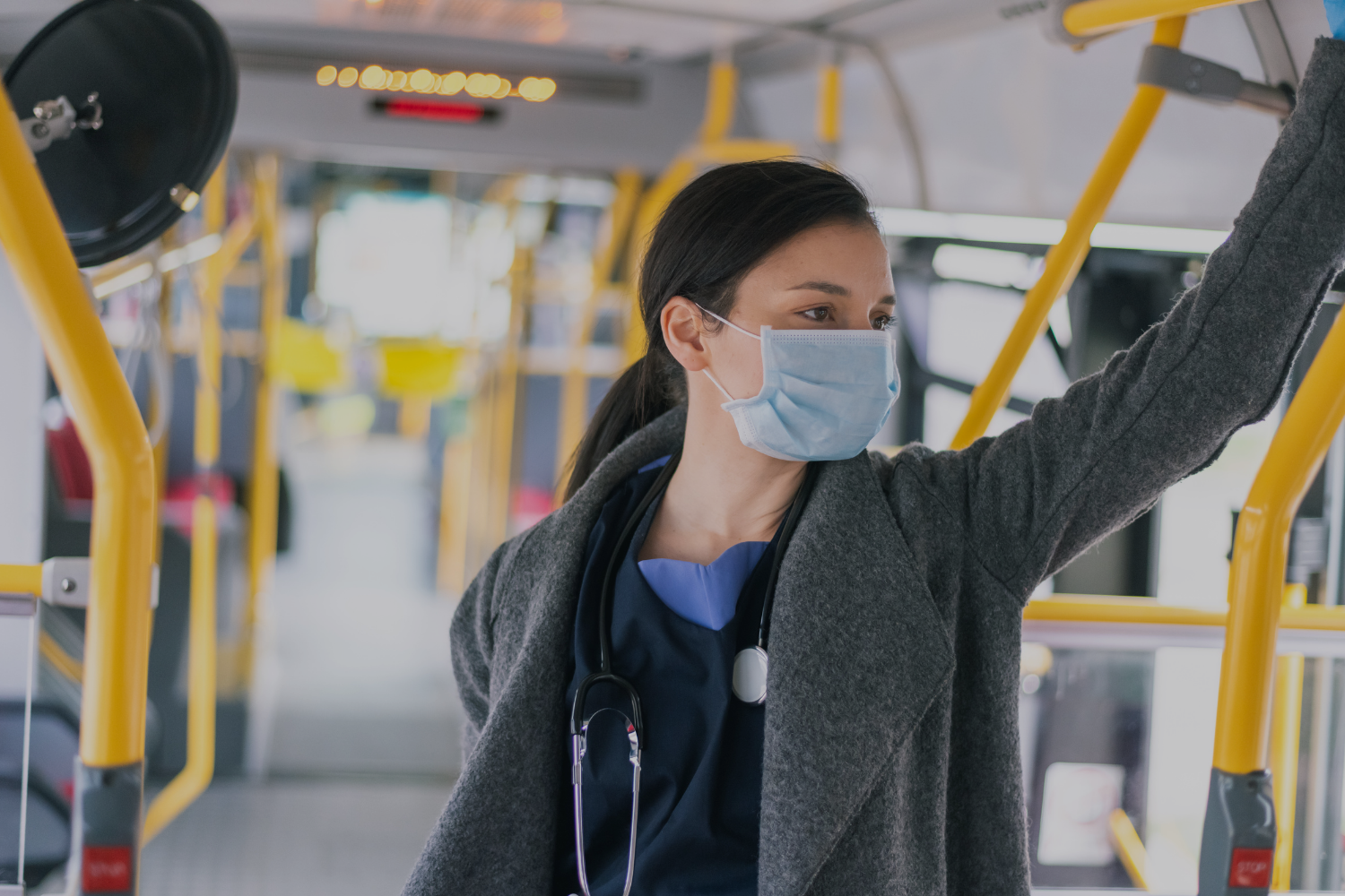 Nurse with stethoscope wearing mask standing on subway train.