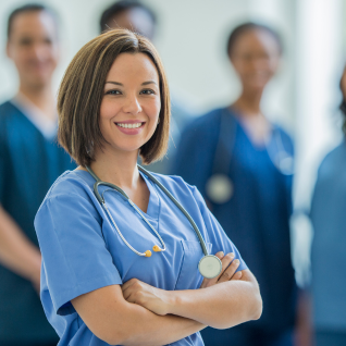 Woman in blue scrubs smiling and standing with her arms crossed